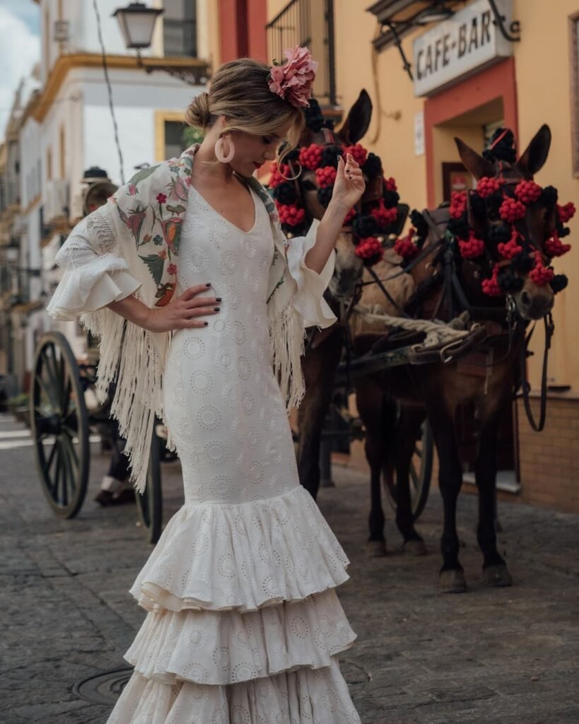 Una mujer paseando en la acera levando puesto un elegante vestido blanco, en el fondo se puede apreciar un carruaje con caballos