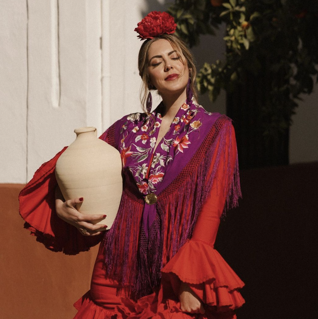 Una mujer con un elegante vestido rojo sostiene en su mano izquierda un jarrón blanco