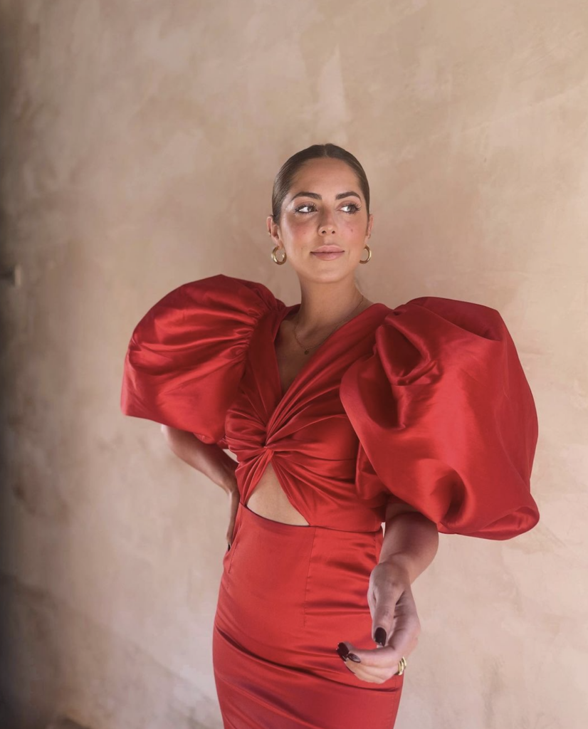 Una mujer recostada en la pared llevando puesto un elegante vestido rojo
