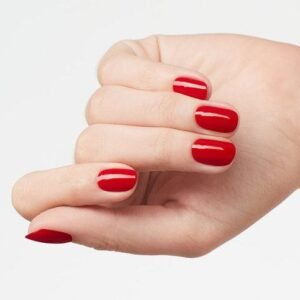 En la imagen una mujer cierra su mano izquierda con sus dedos para hacer resaltar el color rojo de sus uñas brillantes
