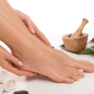 Una mujer masajeando sus pies, en la imagen tambien se muestra unos rollos de tuallas y al fondo un cuenco de arcilla para moler