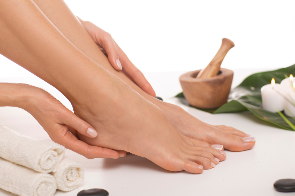 Una mujer masajeando sus pies, en la imagen tambien se muestra unos rollos de tuallas y al fondo un cuenco de arcilla para moler