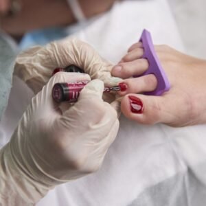 Un especialista haciendo un tratamiento de pedicura pintandole las uñas a una mujer